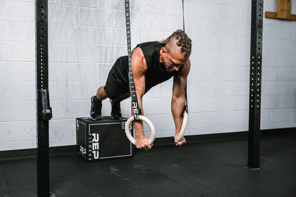 Athlete performing bodyweight pushups on REP Competition Gymnastic Straps and Wood Rings from a REP Soft Plyo box
