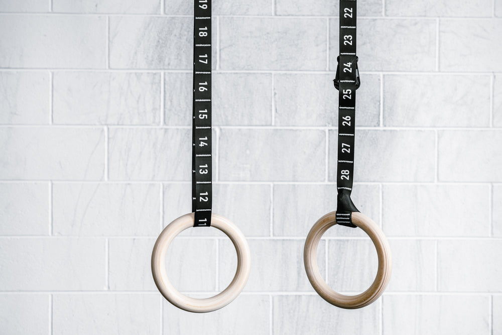 REP’s Competition Gymnastic Straps and Wood Rings hanging in front of a gym wall