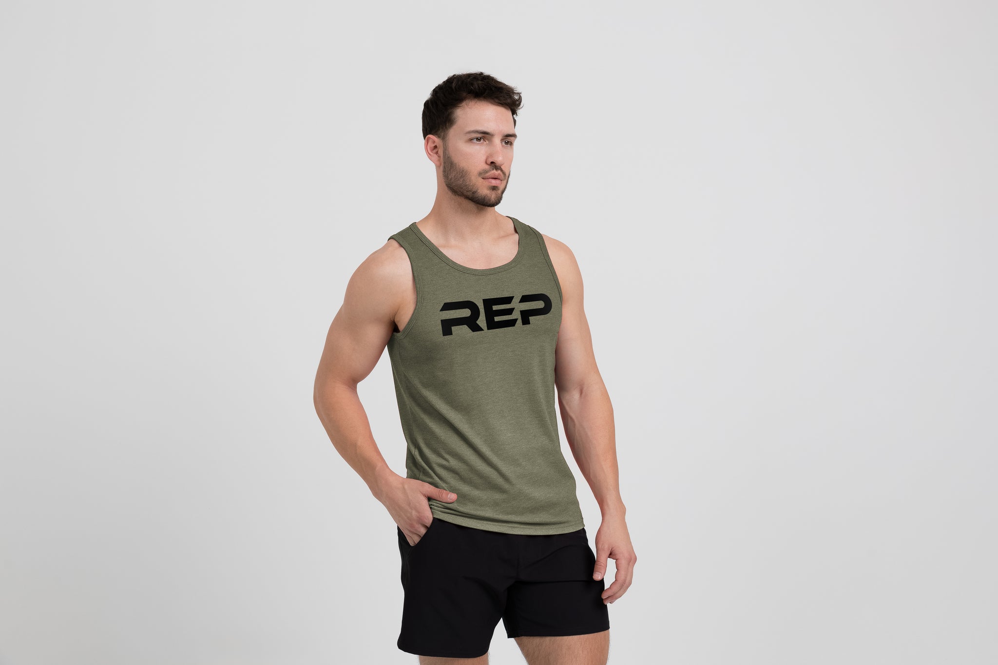 Man wearing the Men's Daily Driver Tri-Blend Tank in Heather Olive with shorts