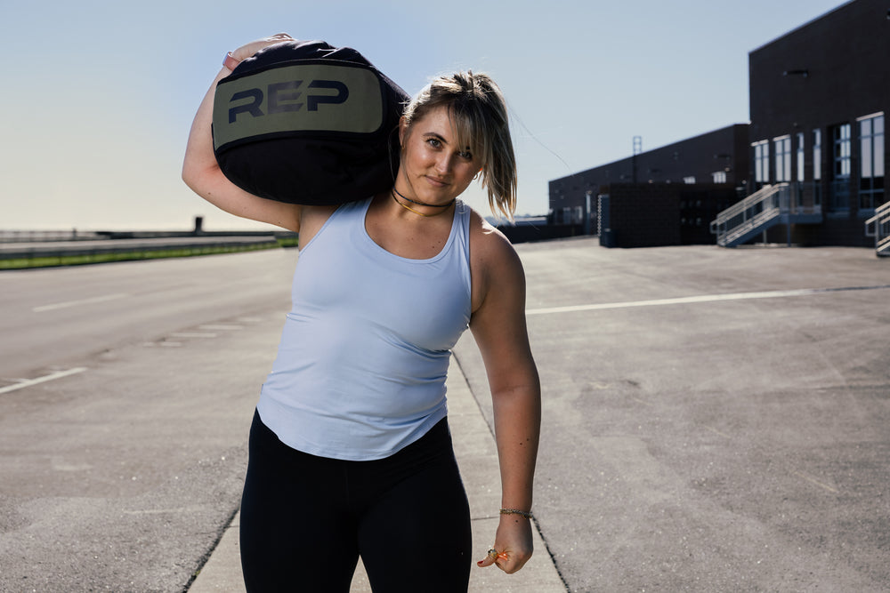 Woman holding REP stone sandbag on shoulder in an outdoor setting.