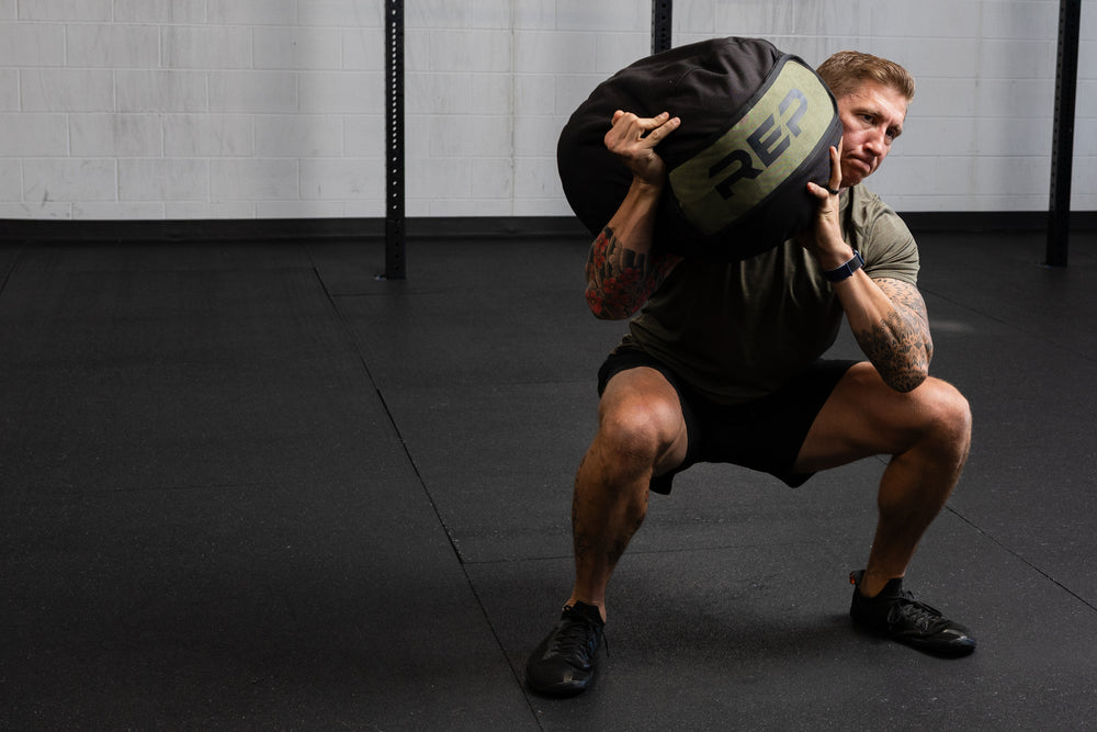 Person performing a squat with a weighted stone sandbag in a gym setting