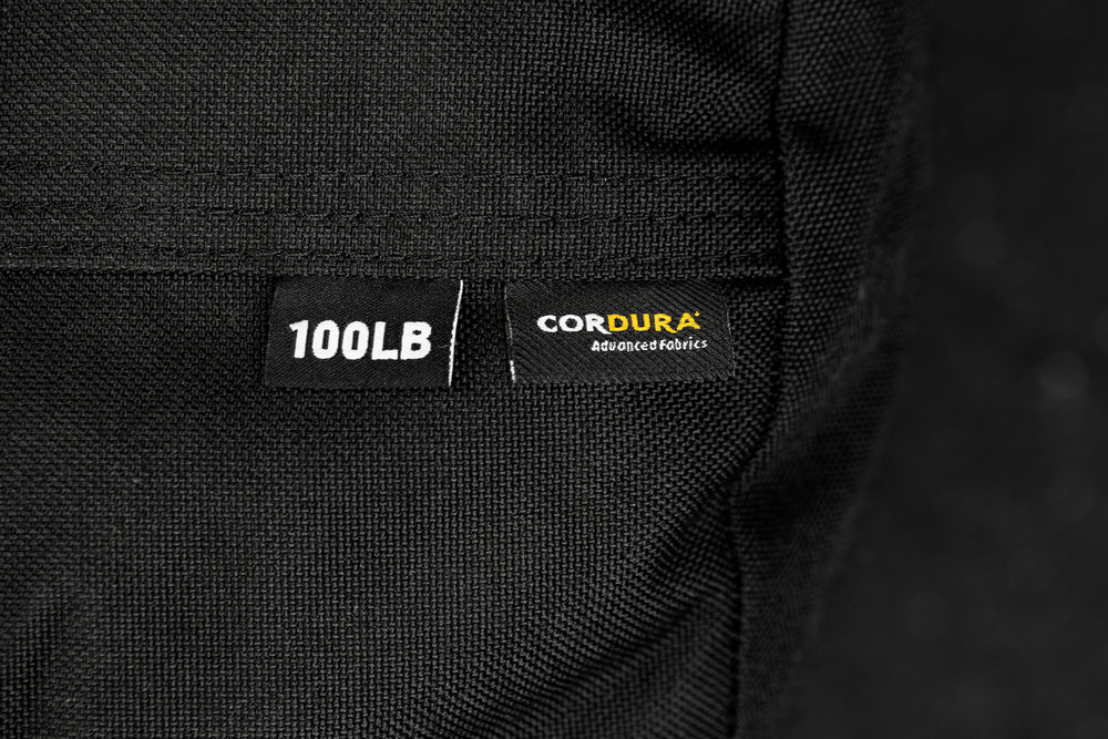 Close-up of a black fabric with '100LB' and 'Cordura' labels on a dark background

