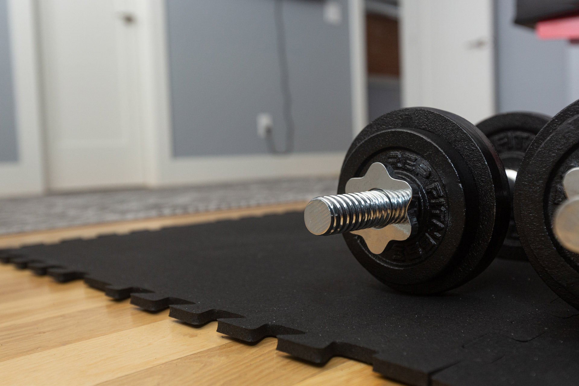 Close up of adjustable dumbbells sitting on top of Rubber Floor Tiles on a wood floor.