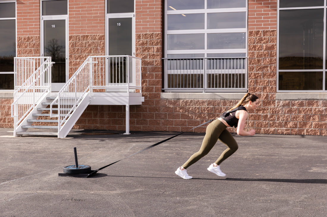 Woman utilizing Sled Harness to pull a sled with weight outside.