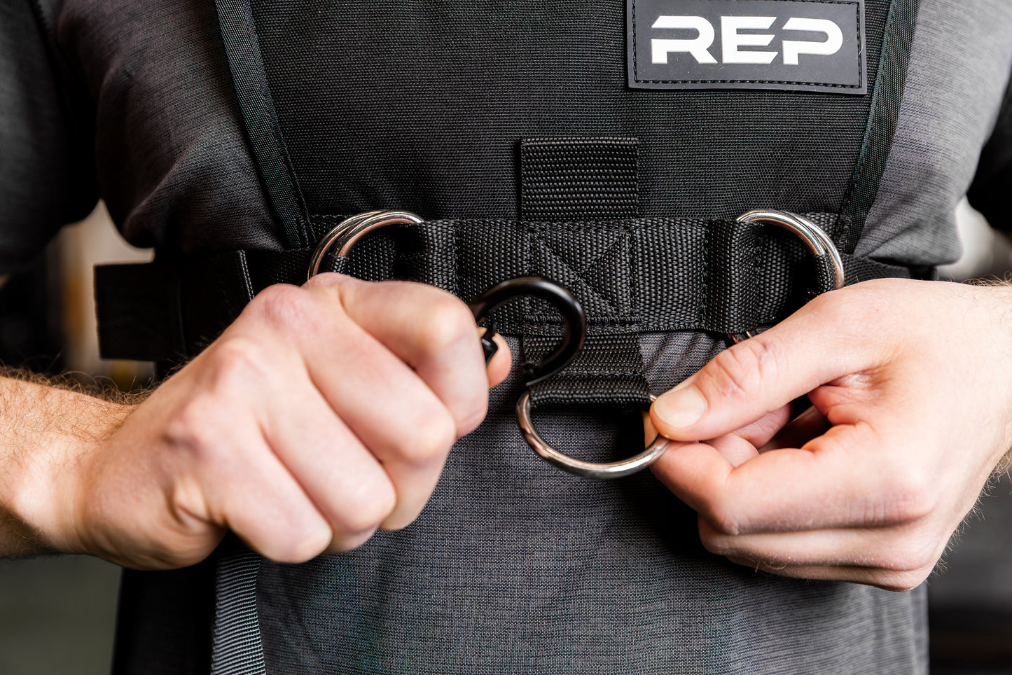 Person adding the Pull Strap to the front of the Sled Harness with 'REP' branding on a blurred background

