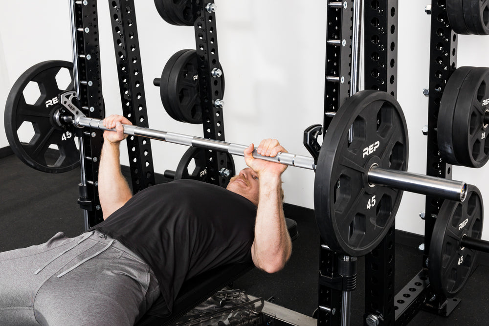 Athlete bench pressing on the front of a rack mounted Smith Machine