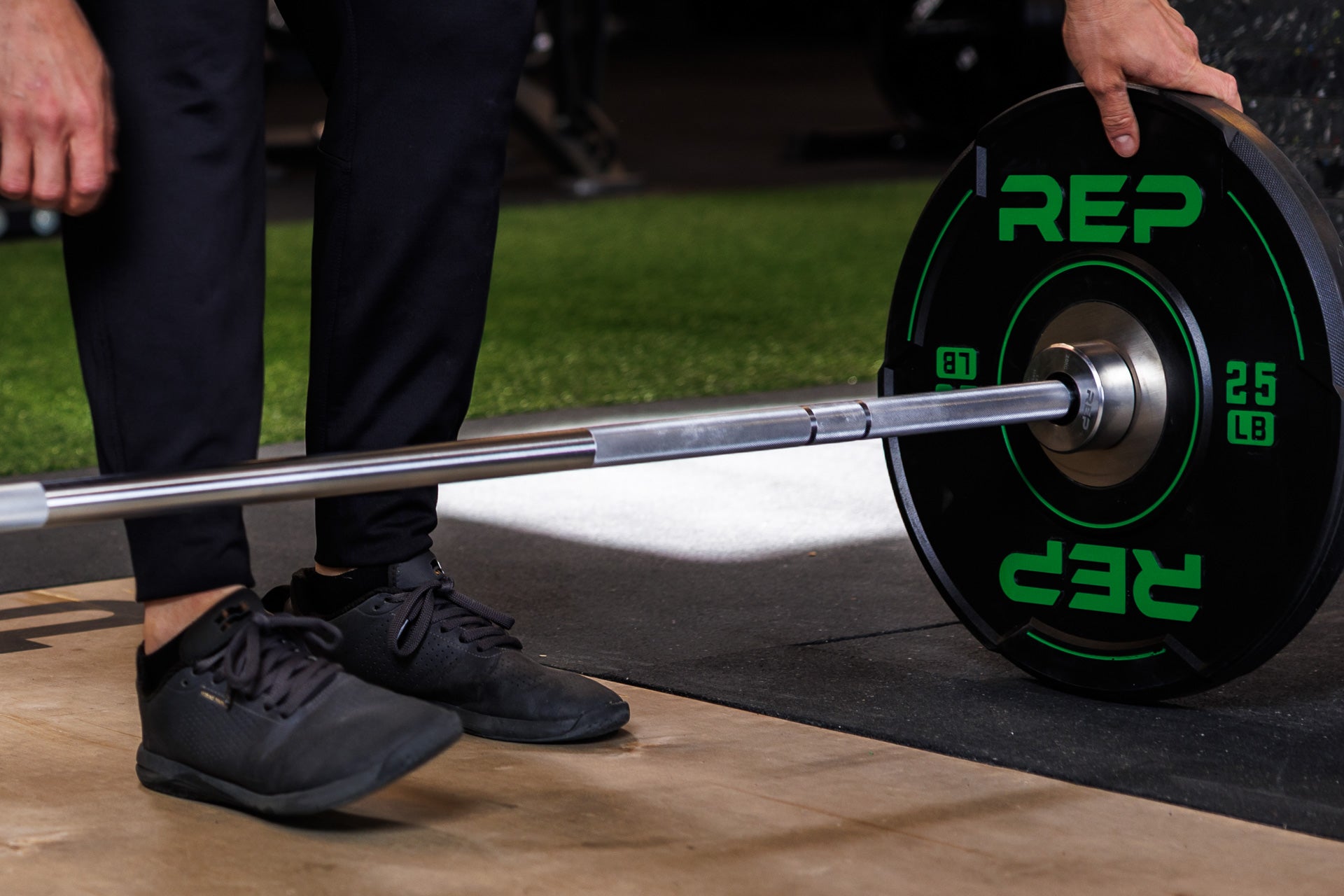 Close-up: Athlete secures a 25 lb REP Sport Bumper Plate 2.0 against a barbell collar, resting on the floor