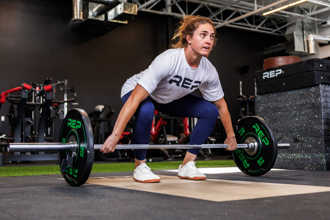 Action-shot: Athlete in a ready position grips a barbell loaded with a pair of REP 25 lb Sport Bumper Plates 2.0