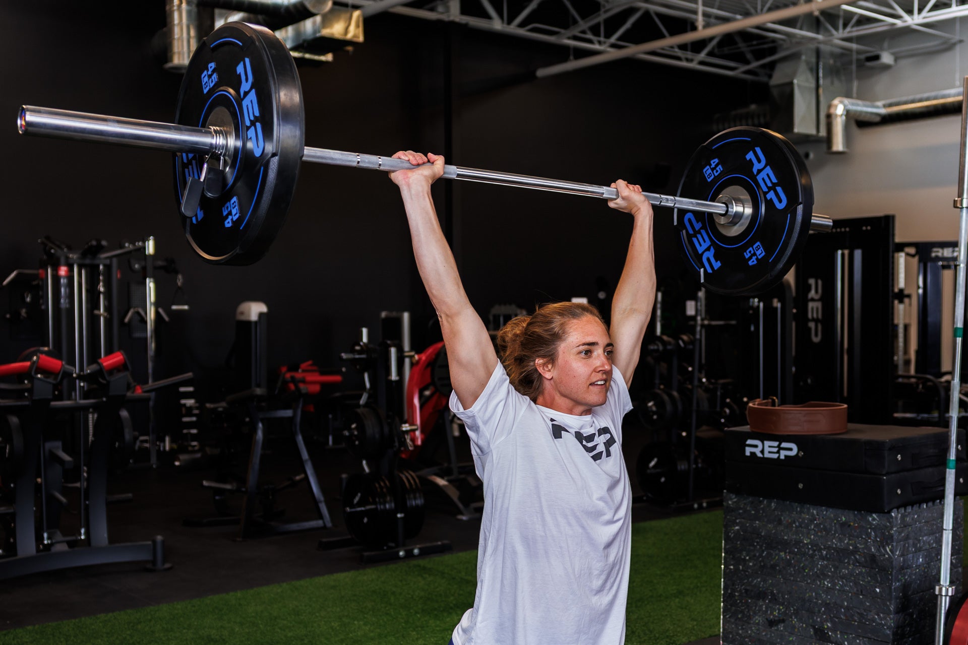 Action-shot: Athlete locks out an overhead lift of a barbell loaded with a pair of REP 45 lb Sport Bumper Plates 2.0