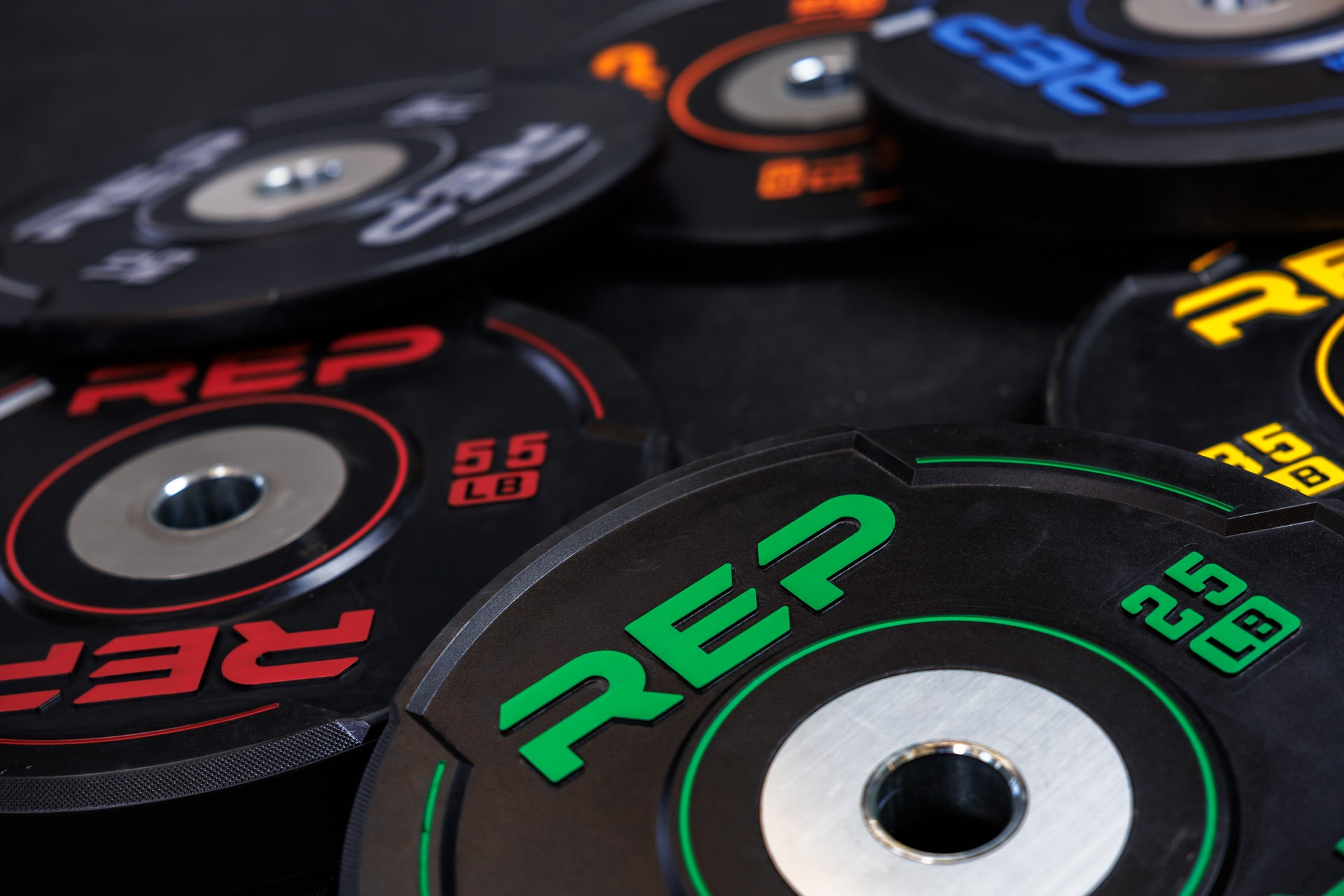Close-up: A creative composition of one of each of the 10, 15, 25, 35, 45, and 55 lb REP Sport Plates 2.0 laying in a pile