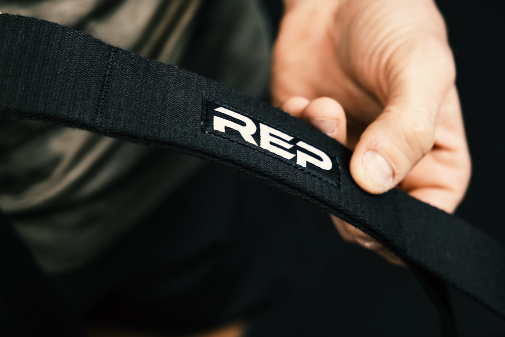Black stretching strap with 'REP' logo held by a person against a dark background