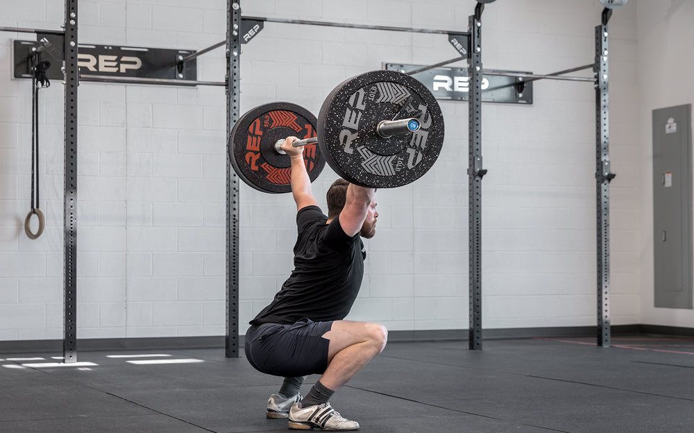 Side view of a male lifter in the bottom catch position of a snatch using a loaded REP Teton Training Bar - 20kg.