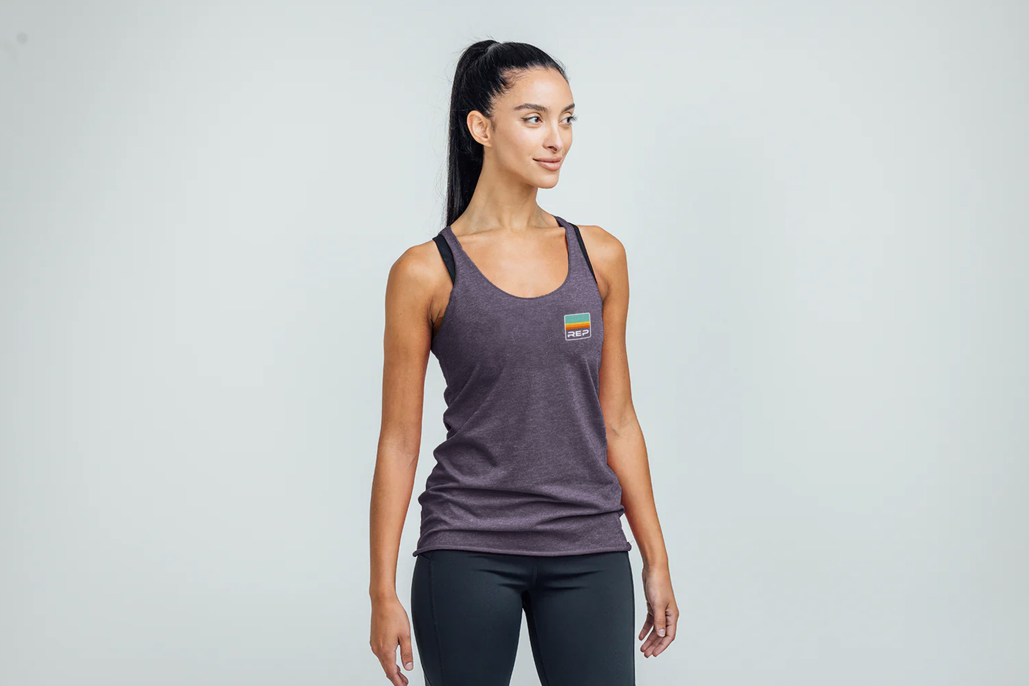 Woman wearing a Rise Tri-Blend Tank in purple with a logo on a gray background
