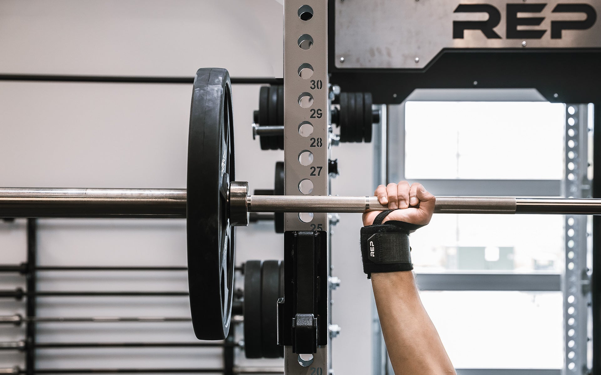 Close-up: Athlete's wrist being supported by the REP Wrist Wrap while pressing a loaded barbell