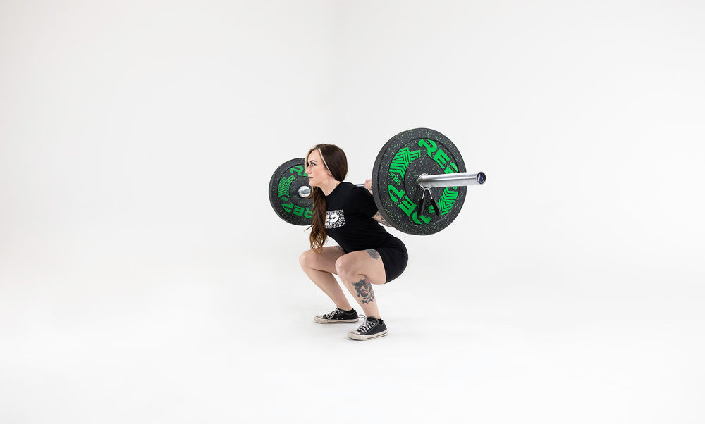 Side view of a lifter in the bottom position of a squat with a barbell in the back rack position loaded with a pair 25lb pinnacle bumper plates.