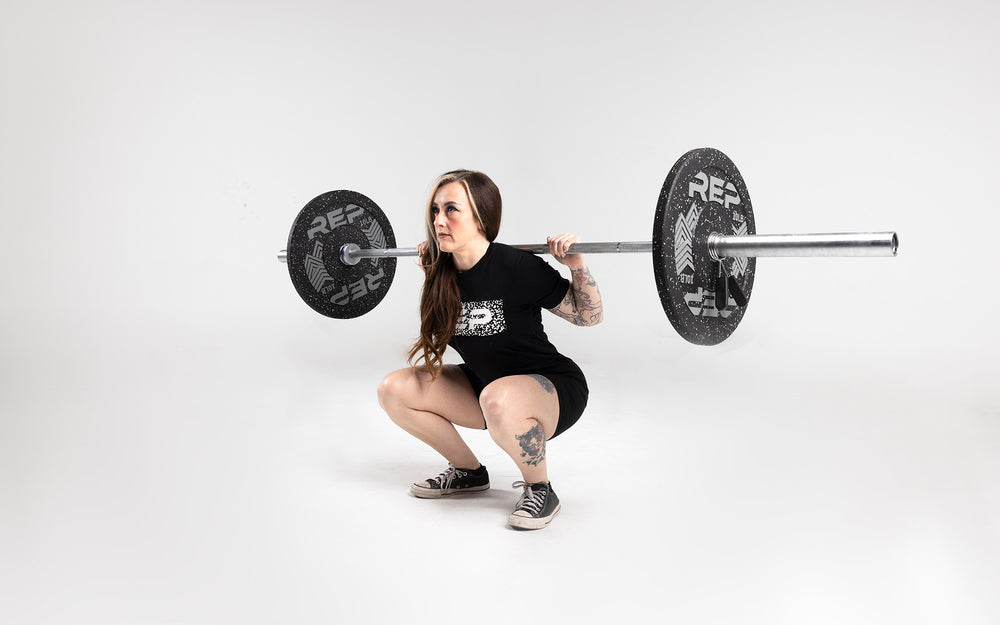 Lifter in the bottom position of a squat with a barbell in the back rack position loaded with a pair of 10lb pinnacle bumper plates.