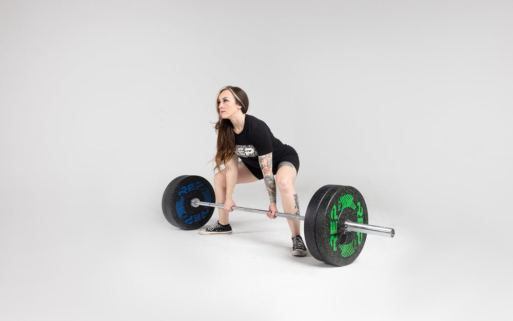 Lifter in the set-up position about to perform a sumo stance deadlift with a barbell loaded with a pair of 25 and 45lb pinnacle bumper plates.