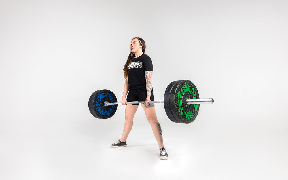 Lifter in the top position after performing a sumo stance deadlift with a barbell loaded with a pair of 25 and 45lb pinnacle bumper plates.