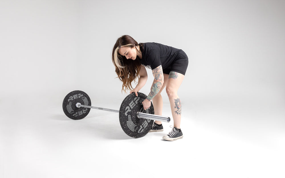 Lifter putting a spring clip on a barbell on the ground loaded with a pair of 10lb pinnacle bumper plates.