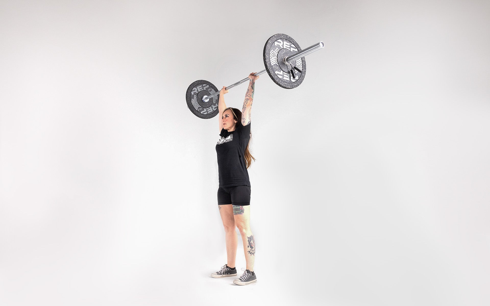 Lifter in the finish position of a shoulder press with a barbell overhead loaded with a pair of 10lb pinnacle bumper plates.