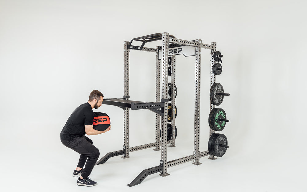 Utility Seat Installed on Spotter Arms on Power Rack Being Used for Stone Sandbag Exercises