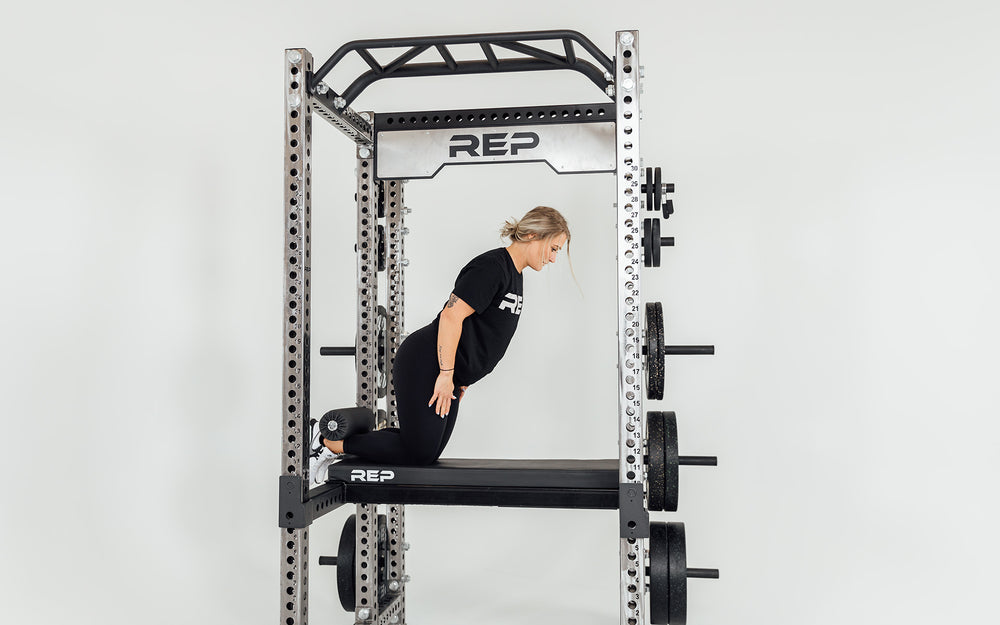 Utility Seat + Pad Installed on Flip-Down Safeties  on Power Rack Being Used for Nordic Curls