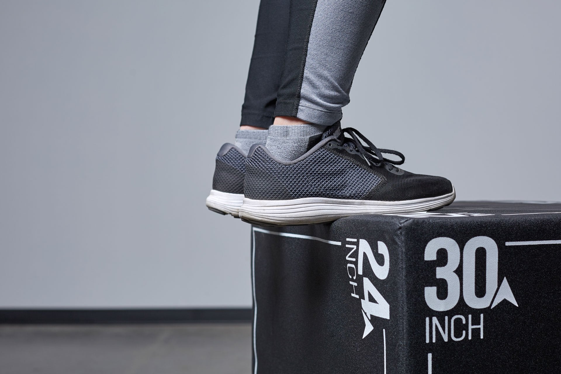 Close-up view of an individual's feet on top of a Large REP 3-in-1 Soft Plyo Box.