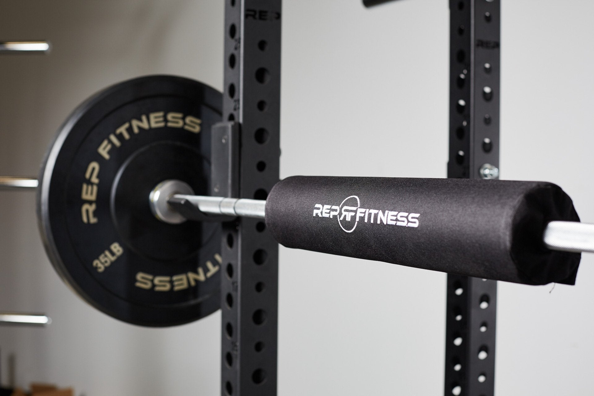 A REP barbell shoulder pad secured onto a racked barbell loaded with REP bumper plates.