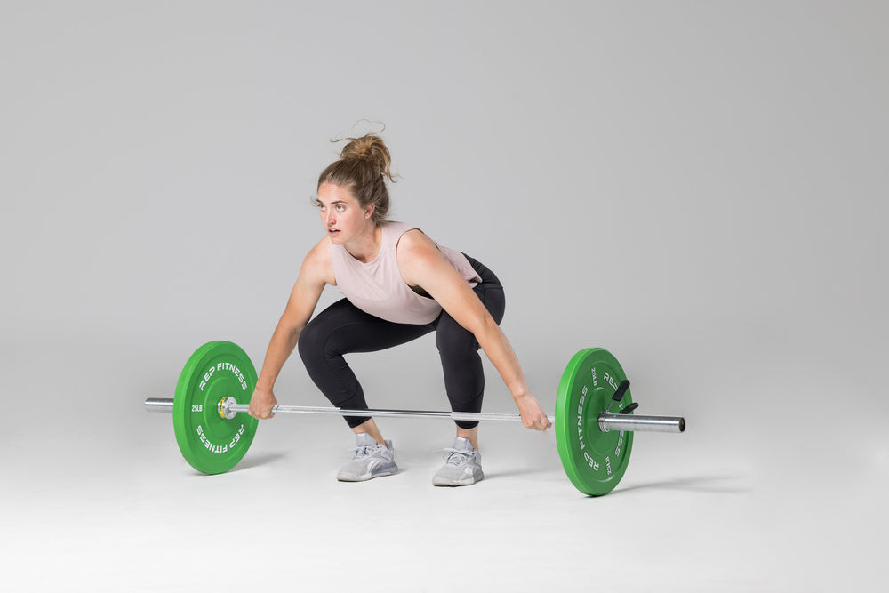 Lifter in set-up position to perform a snatch with a barbell loaded with a pair of green 25lb colored bumper plates.