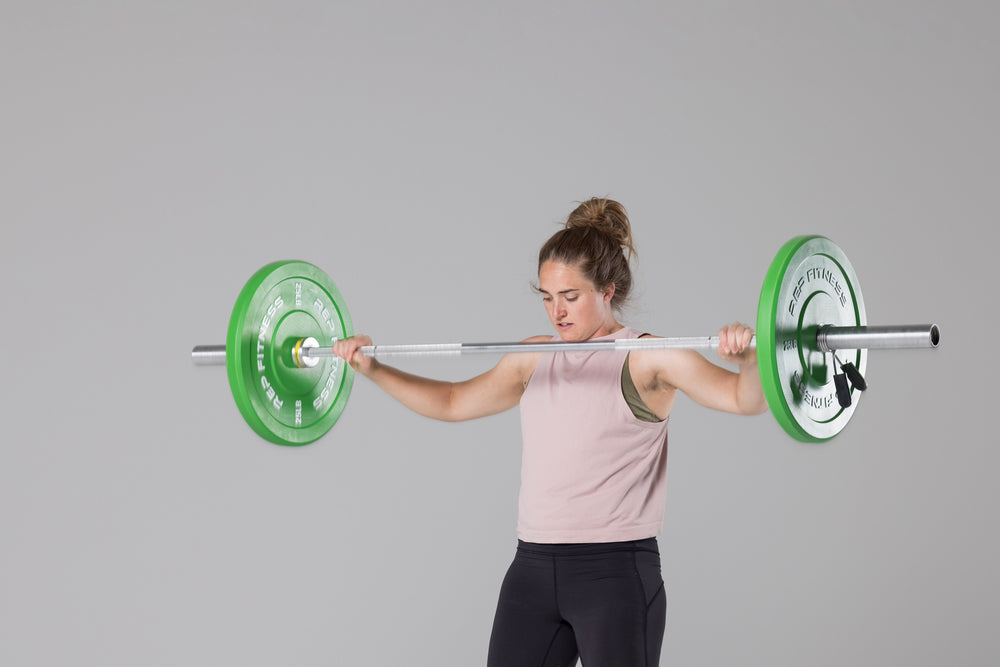 Lifter dropping a barbell loaded with a pair of green 25lb colored bumper plates from shoulder height after having performed a snatch.