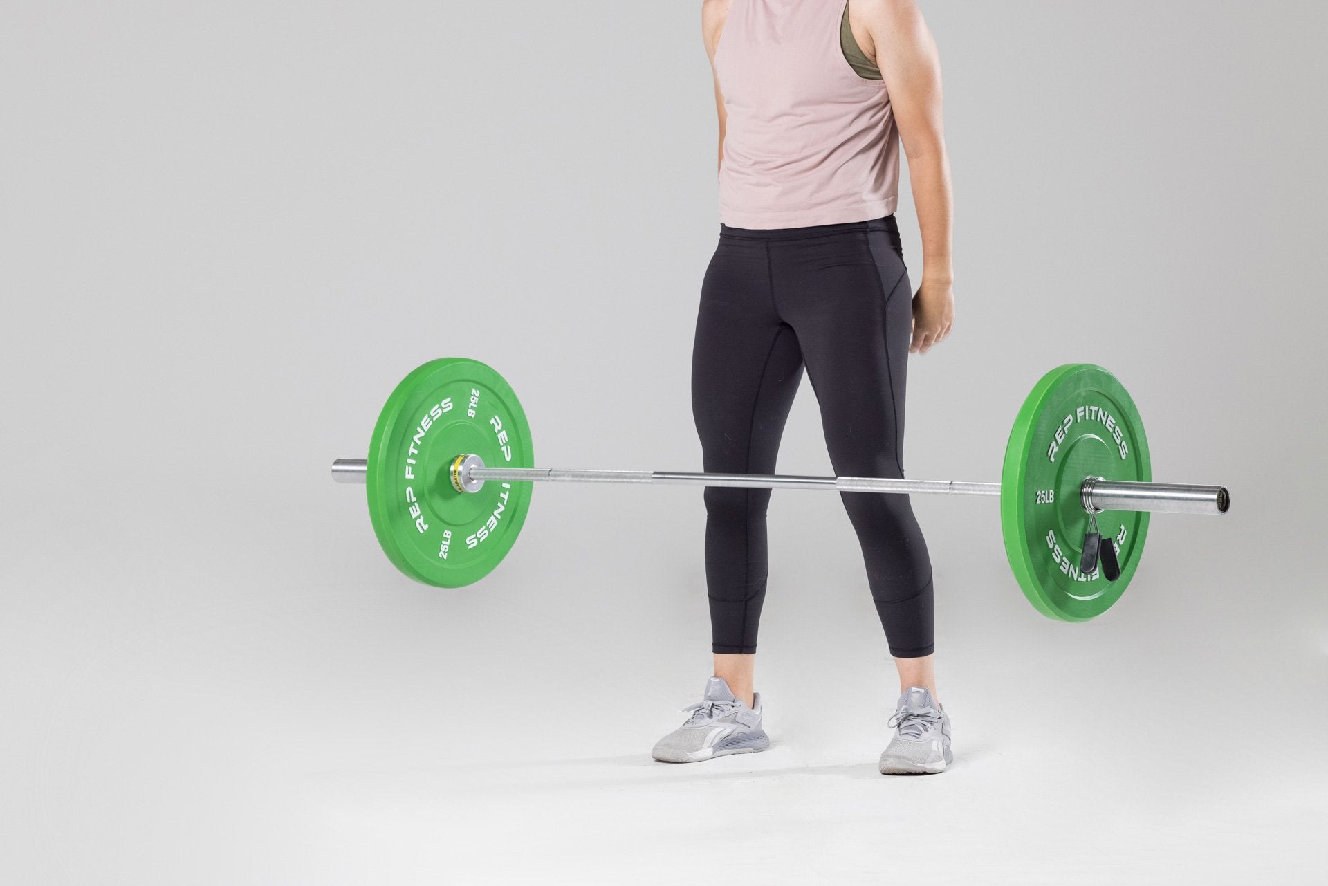 A barbell loaded with a pair of green 25lb colored bumper plates falling to the ground after being dropped by a lifter.