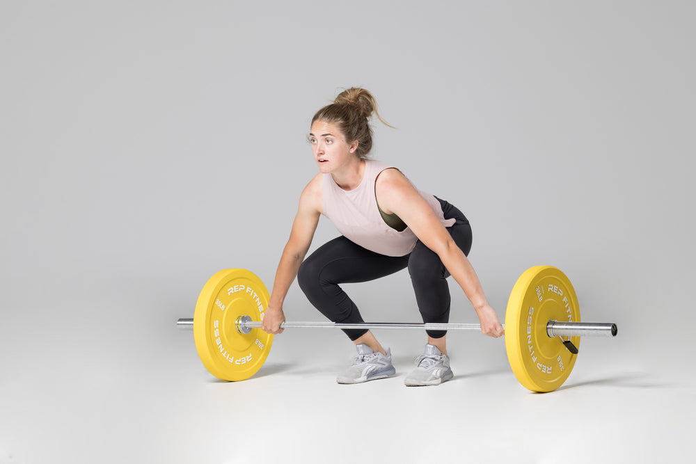 Lifter in set-up position to perform a snatch with a barbell loaded with a pair of yellow 35lb colored bumper plates.