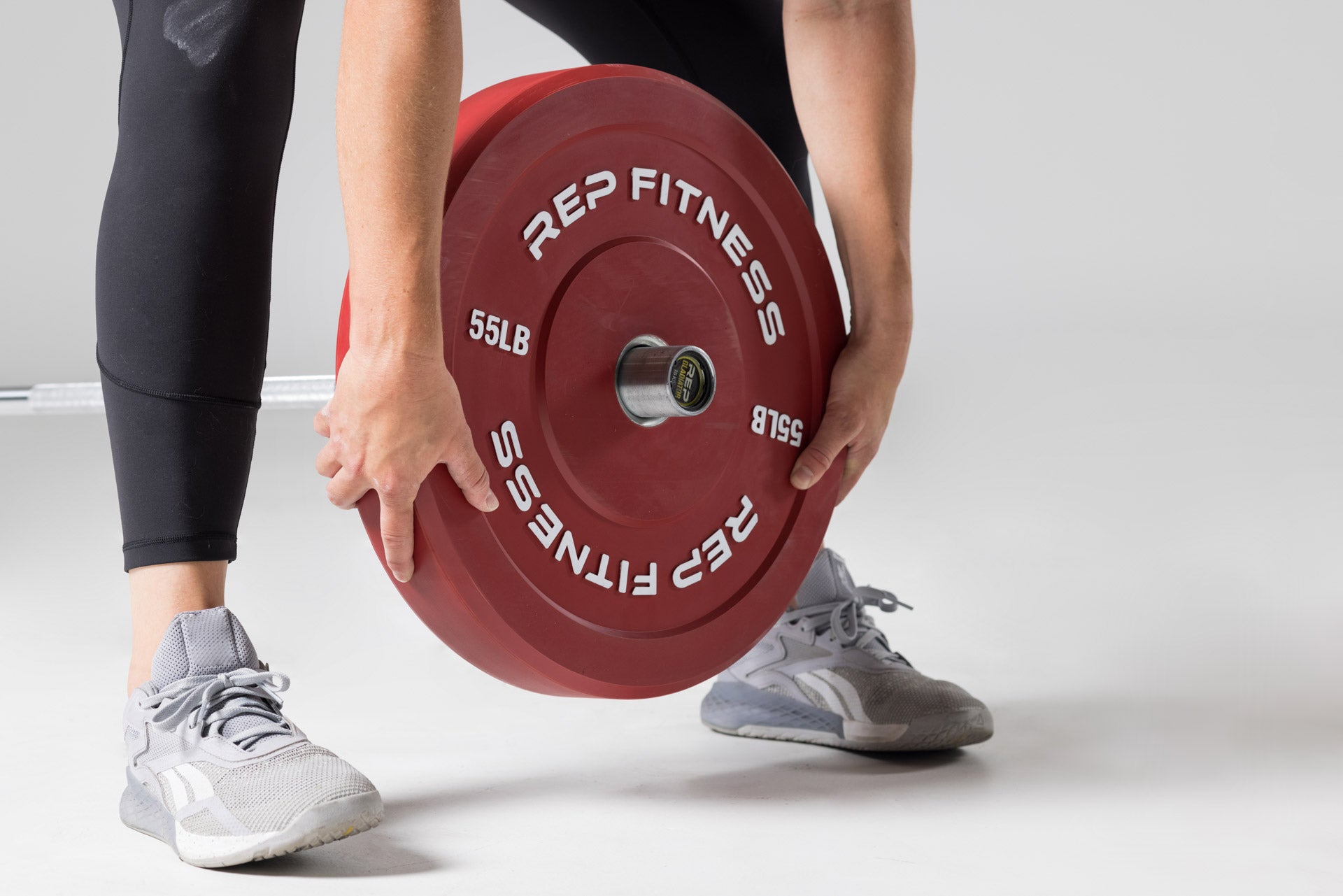 Close-up view of a lifter loading a red 55lb colored bumper plate onto a barbell on the floor.