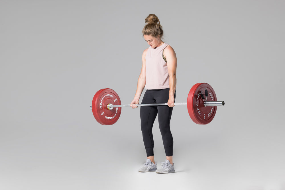 Lifter at the top position of a deadlift using a barbell loaded with a pair of red 55lb colored bumper plates.