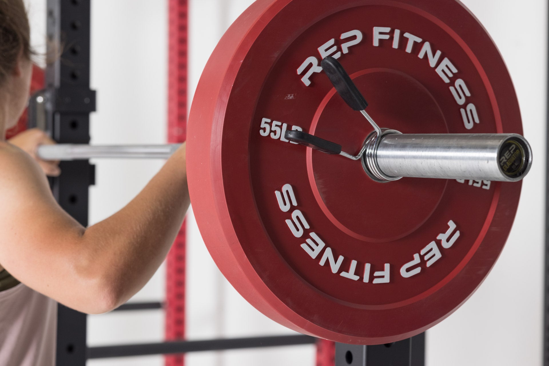 Close-up view of a red 55lb colored bumper plate loaded on a barbell that is racked on j-cups in a REP power rack.