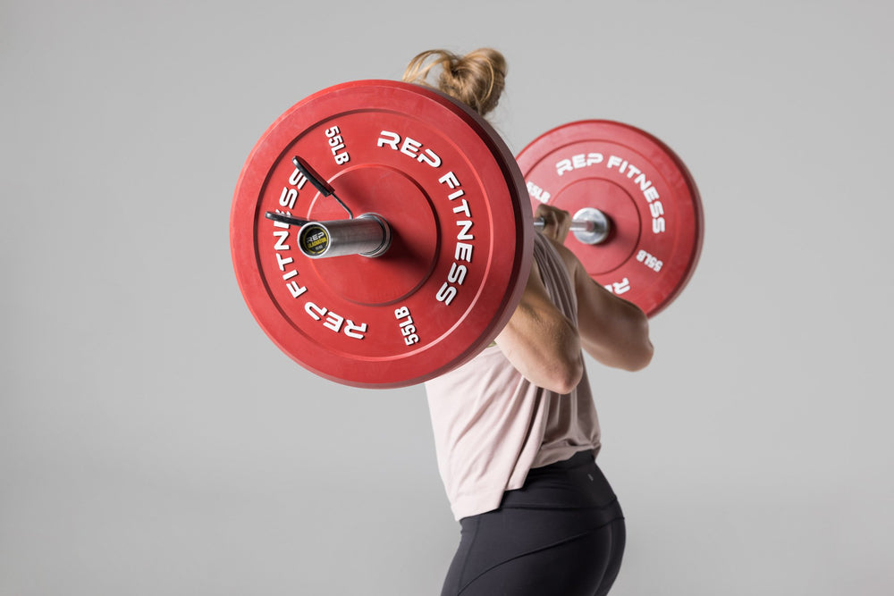 Side view of a lifter with a barbell in the back rack position that is loaded with a pair of red 55lb colored bumper plates.