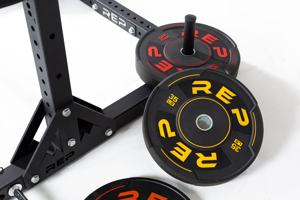 View of the back of a REP squat rack with a 55lb sport bumper plate on the weight peg and a 35lb sport bumper plate next to it.