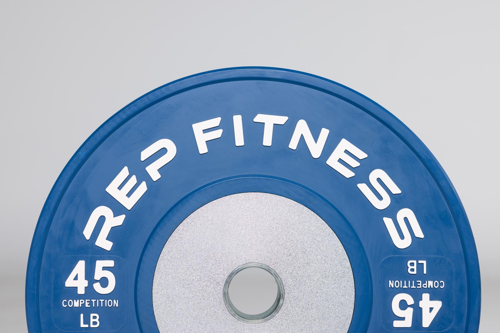 Close-up view of half of a blue 45lb competition bumper plate showing zinc-coated steel disc insert and raised white 