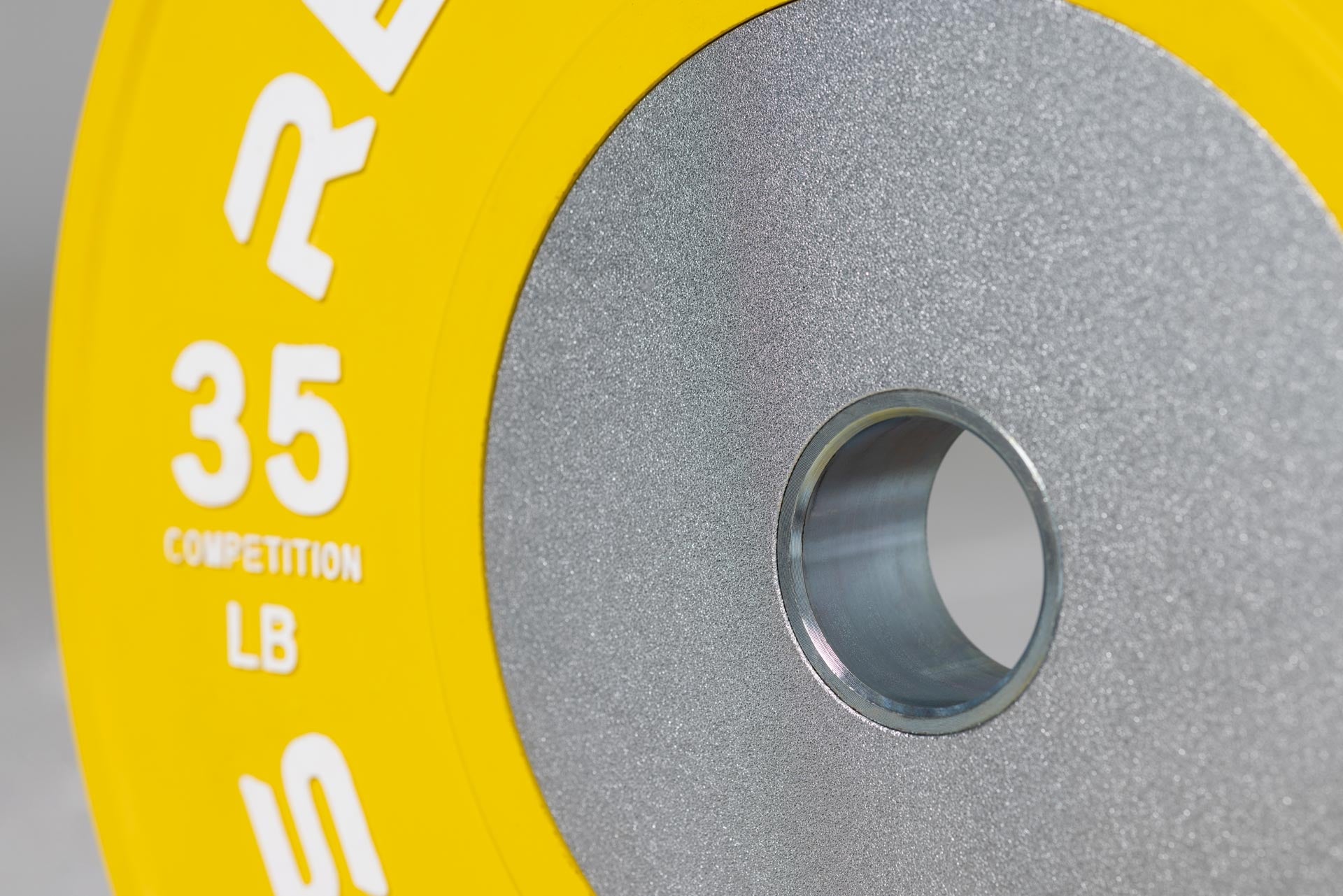 Close-up view of a yellow 35lb competition bumper plate showing zinc-coated steel disc insert and raised white weight marking lettering.