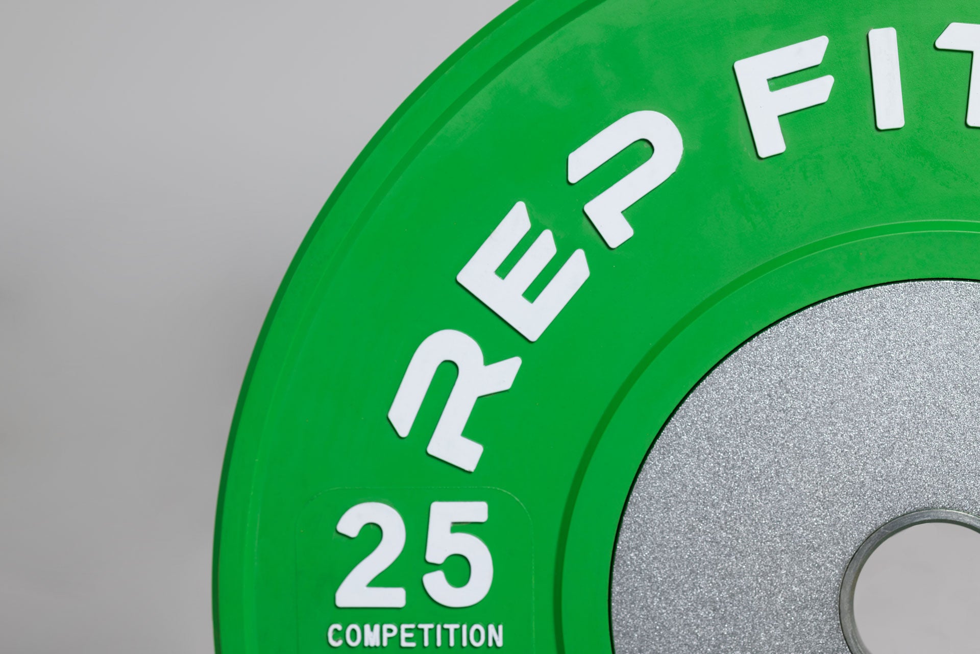 Close-up view of a green 25lb competition bumper plate showing zinc-coated steel disc insert and raised white 