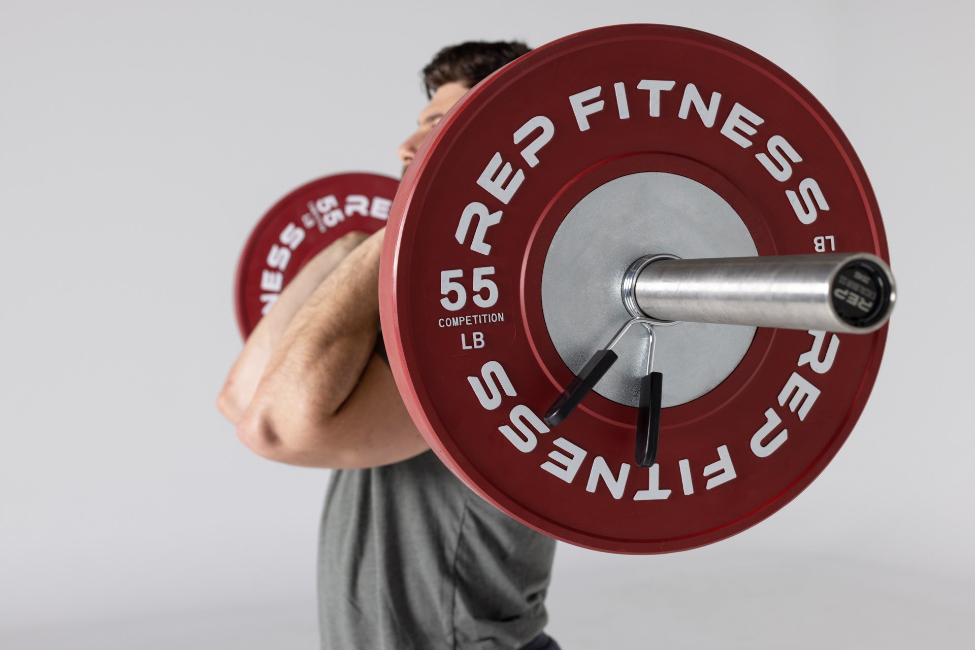 Side view of a lifter holding a barbell loaded with a pair of red 55lb competition bumper plates in the front rack position.