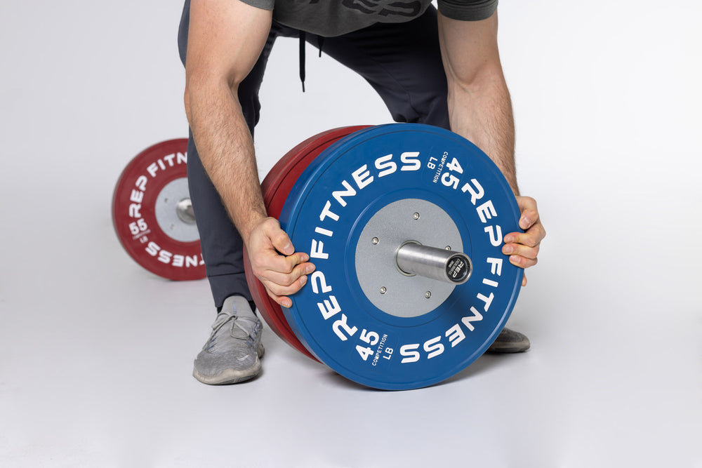 Side view of a lifter loading a blue 45lb competition bumper plate onto a barbell on the ground.