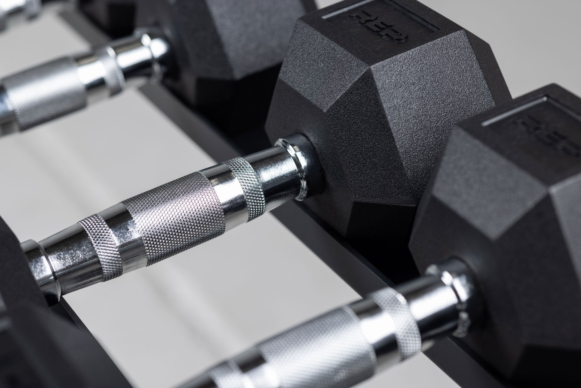 Close-up view of the ergonomic handles and hexagon heads of a pair of Ergo Hex Dumbbells being stored on a REP Dumbbell Rack.