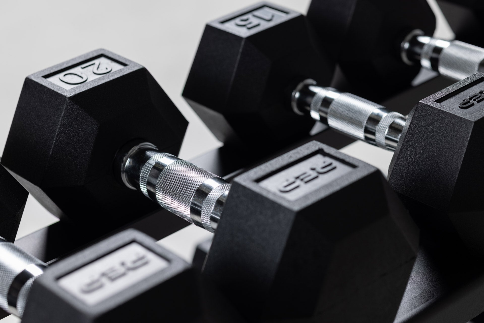 Close-up view of a pair of 15 and 20lb Ergo Hex Dumbbells being stored on the top shelf of a REP Dumbbell Rack.
