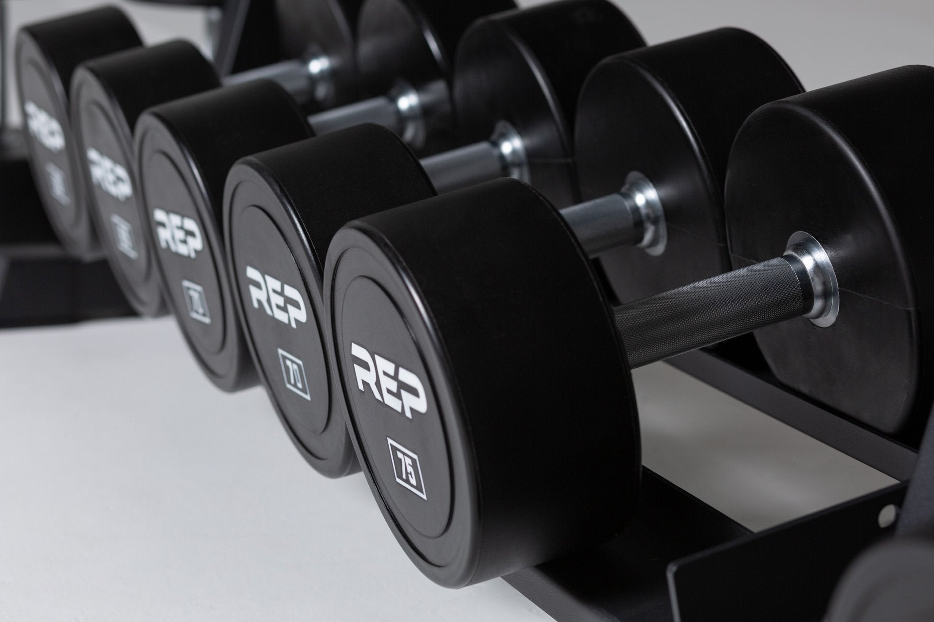 Close-up view of the 75lb pair of a 5-75lb Urethane Dumbbell Set being stored on the bottom shelf of a REP Dumbbell Rack.