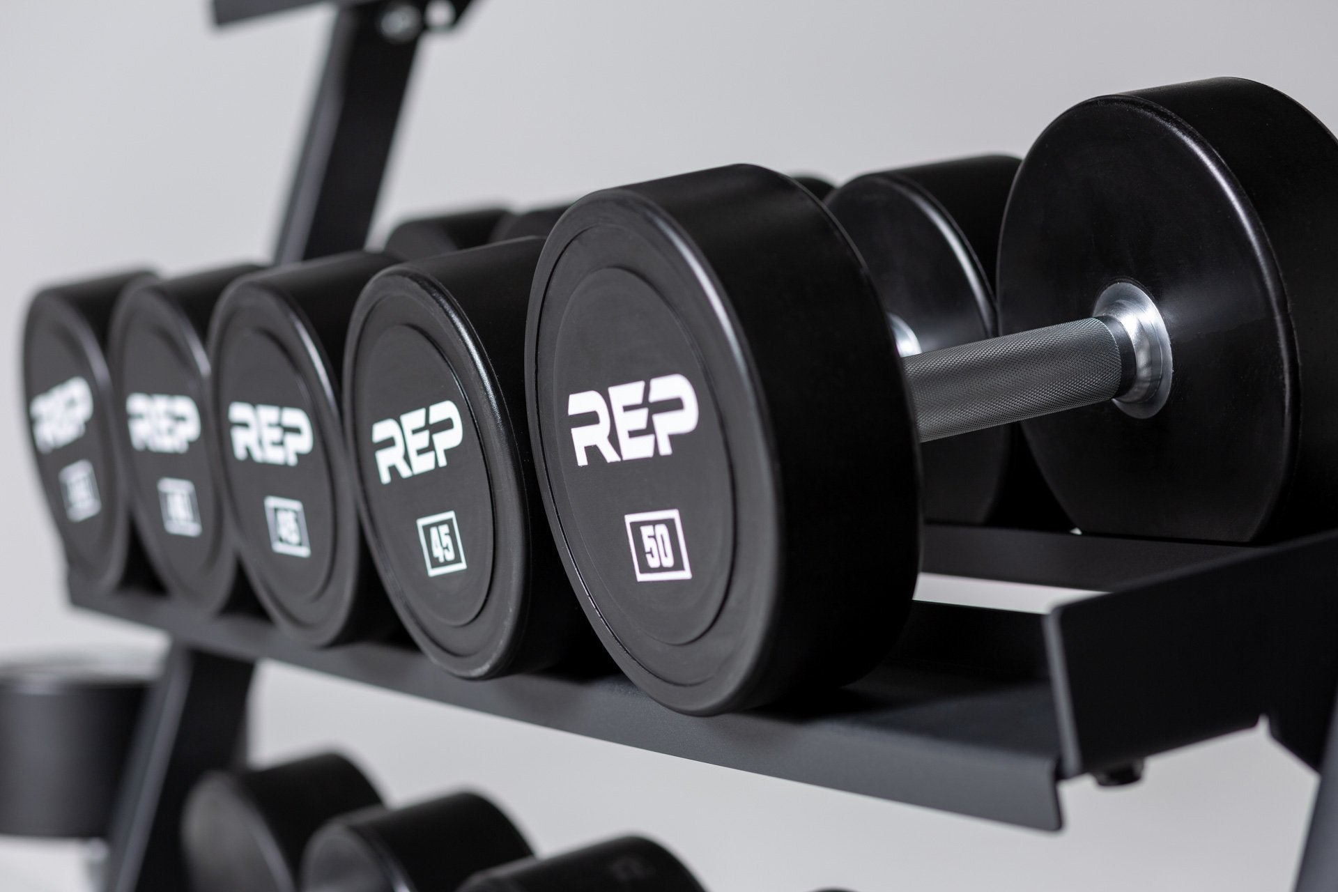 Close-up view of a 45 and 50lb Urethane Dumbbell being stored on the middle shelf of a REP Dumbbell Rack.