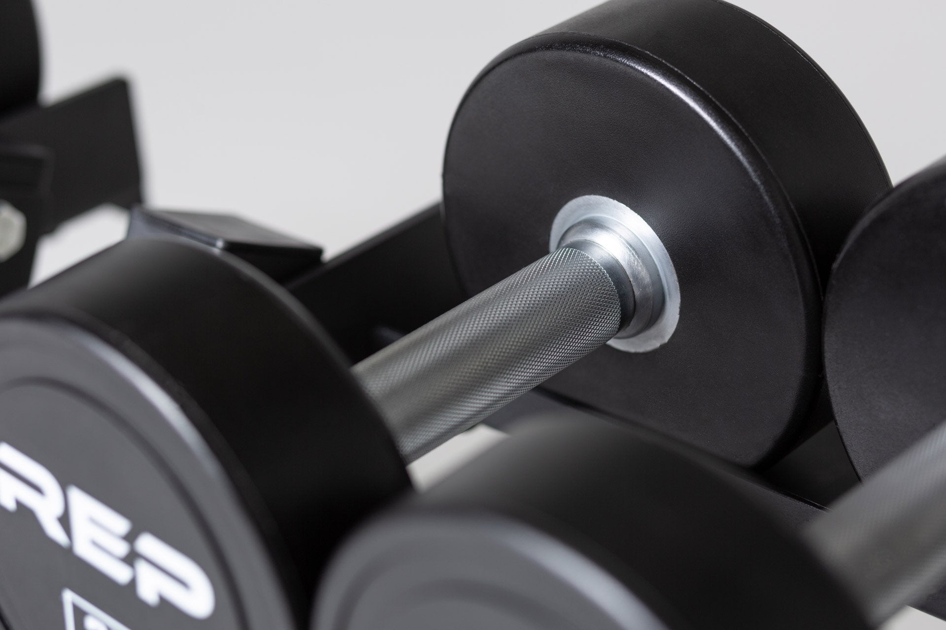 Close-up view of the straight knurled handle and the round head of a Urethane Dumbbell being stored on a REP Dumbbell Rack.