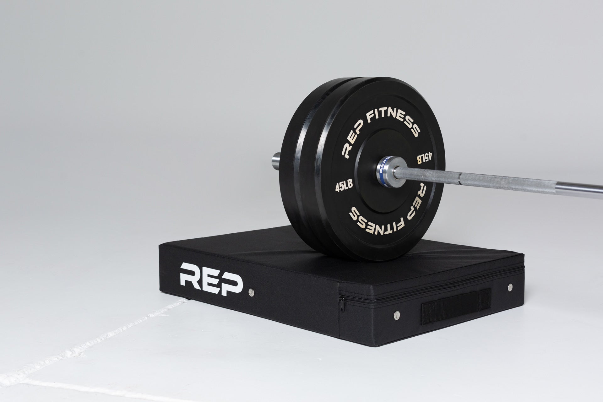 A barbell loaded with two 45lb REP bumper plates resting on the REP Crash Pad.