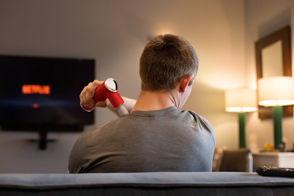 Individual using the Rapidstrike Massage Gun on his trap while watching television.