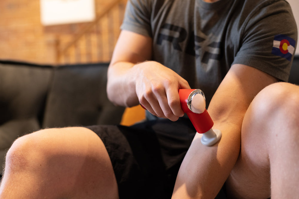 Individual using the Rapidstrike Massage Gun on his upper forearm while sitting on the couch.